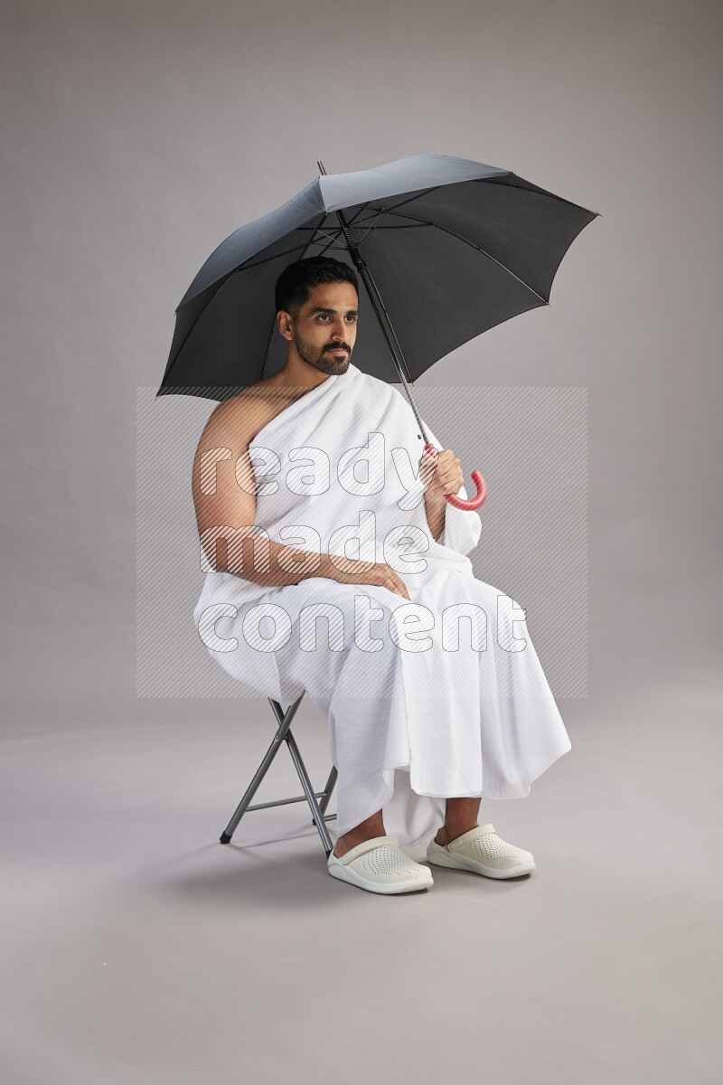 A man wearing Ehram with face mask Standing holding umbrella on gray background