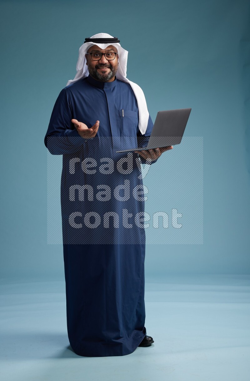 Saudi Man with shimag Standing working on laptop on blue background