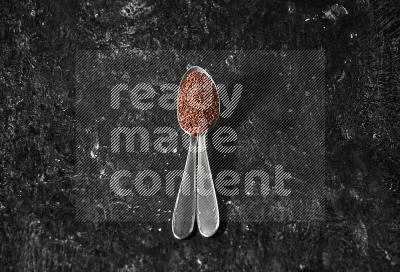 2 metal spoons full of garden cress seeds on a textured black flooring