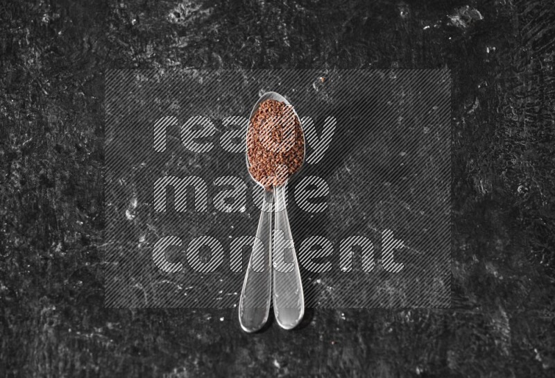 2 metal spoons full of garden cress seeds on a textured black flooring