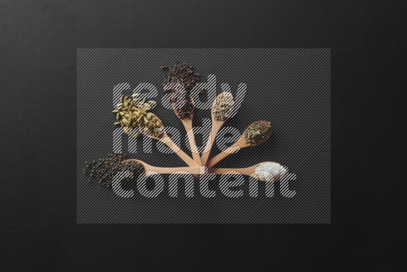 الفلفل الأبيض والقرنفل والهيل والملح والفلفل الأسود وريحان مجفف في معالق خشبية علي خلفية سوداء