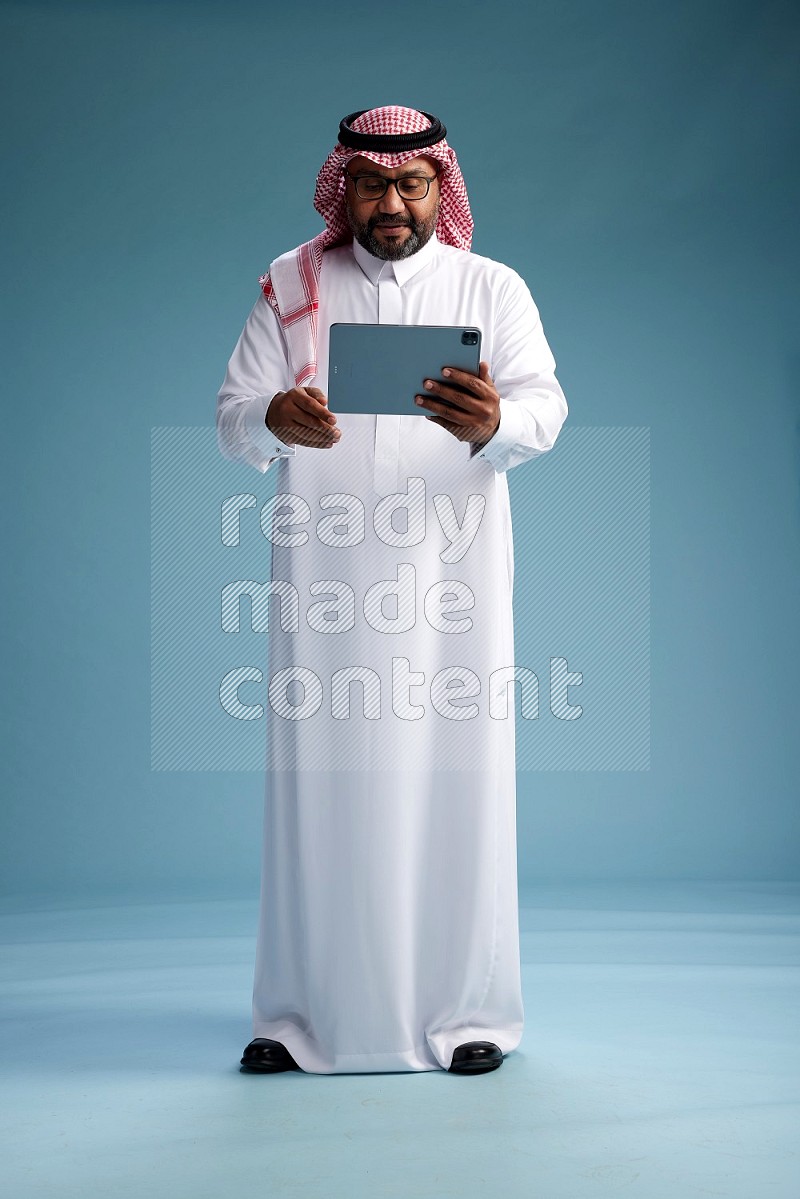 Saudi Man with shimag Standing holding a tablet on blue background