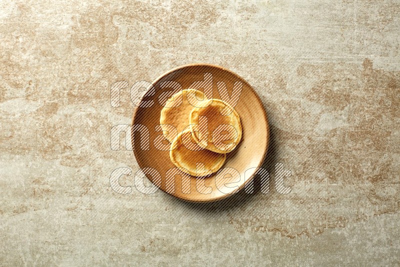 Three stacked plain mini pancakes in a brown plate on beige background
