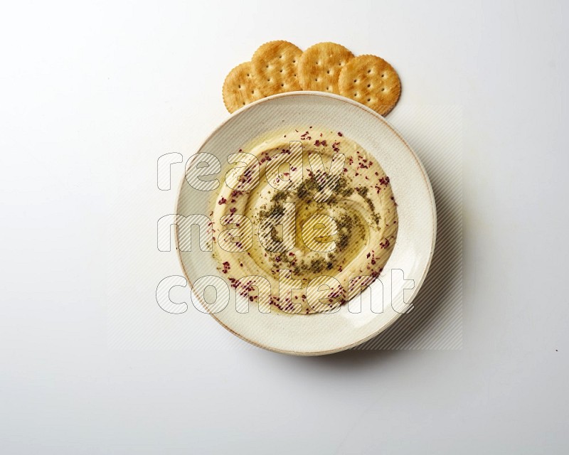 Hummus in a pottry plate garnished with zaatr & sumak on a white background