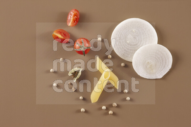 Raw pasta with different ingredients such as cherry tomatoes, garlic, onions, red chilis, black pepper, white pepper, bay laurel leaves, rosemary and cardamom on beige background