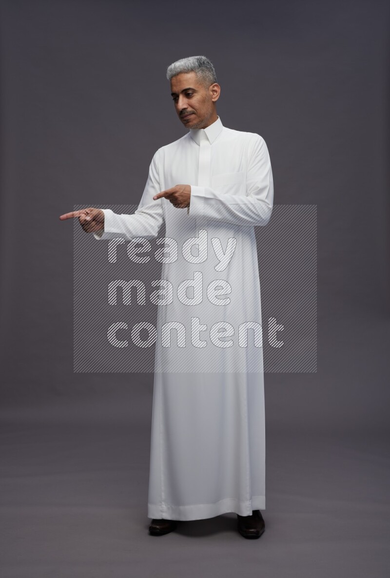 Saudi man wearing thob standing interacting with the camera on gray background