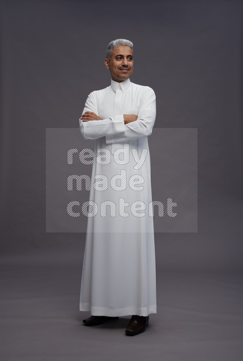 Saudi man wearing thob standing with crossed arms on gray background