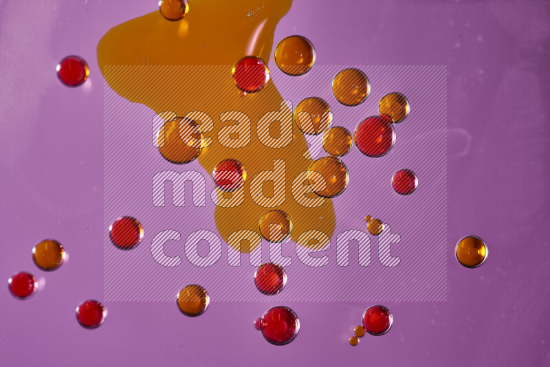 Close-ups of abstract orange and red watercolor drops on oil Surface on pink background