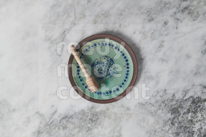 Decorative pottery plate with wooden honey dipper in it on grey marble background
