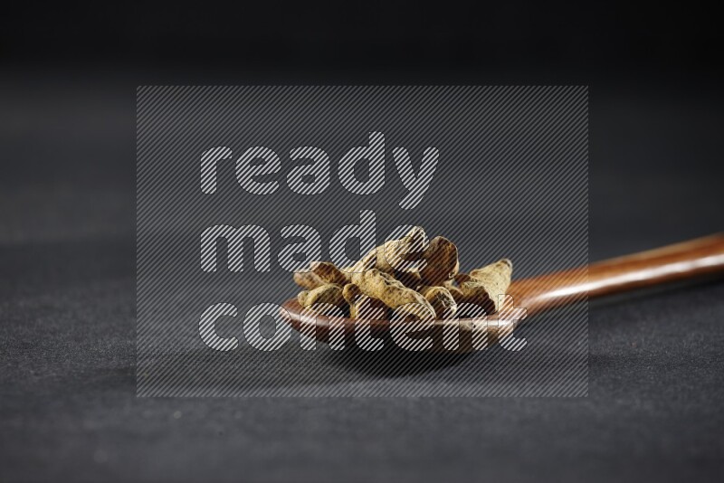A wooden ladle full of dried turmeric fingers on black flooring