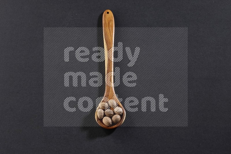 A wooden ladle full of whole nutmeg seeds on a black flooring