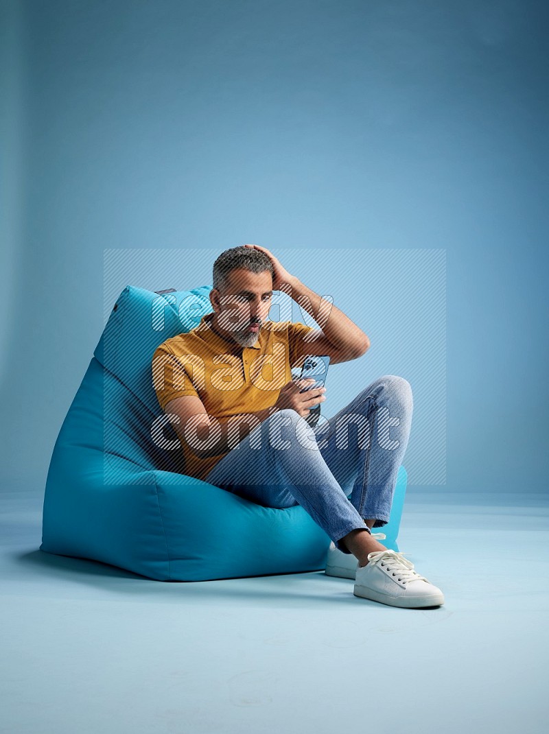 A man sitting on a blue beanbag and texting on phone