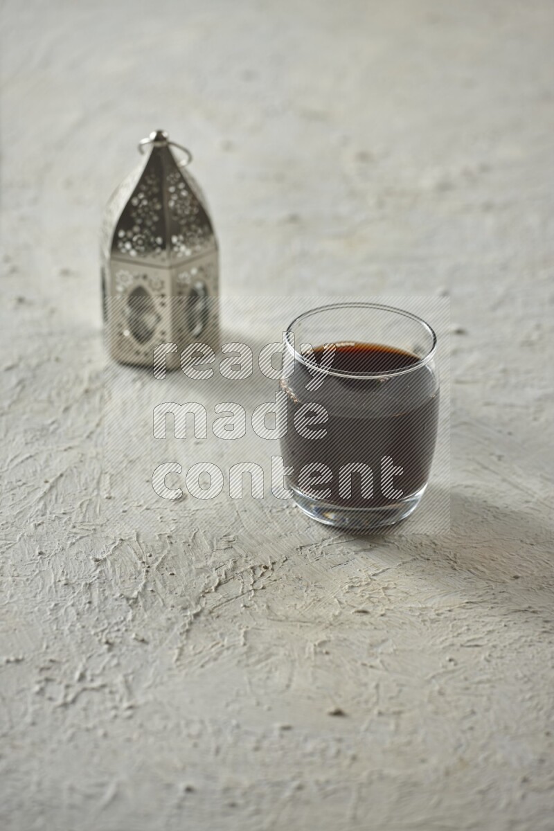 A silver lantern with different drinks, dates, nuts, prayer beads and quran on textured white background