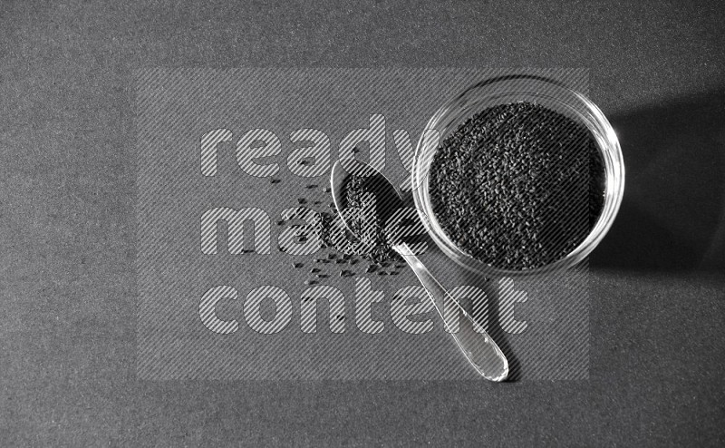 A glass bowl full of black seeds with a metal spoon full of the seeds on a black flooring in different angles