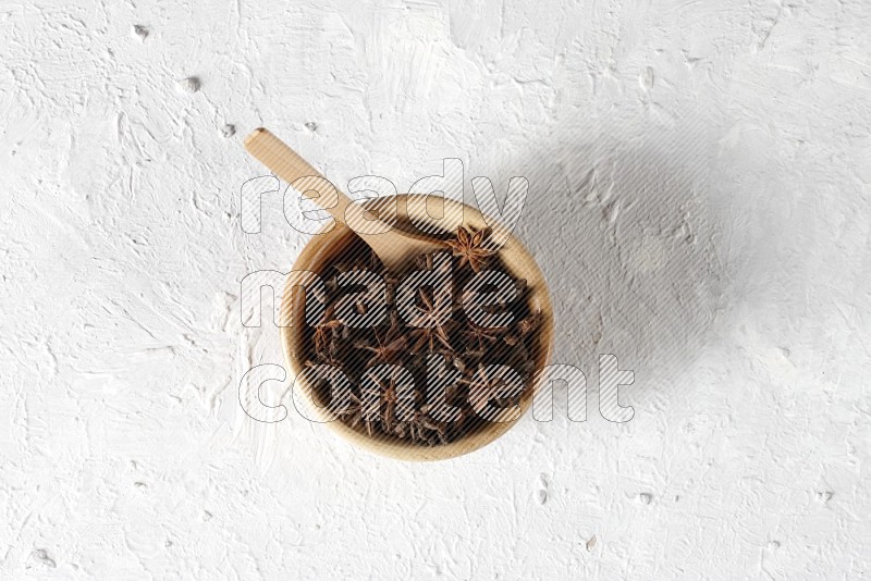 Star anise in a wooden bowl with a wooden spoon in it on white background