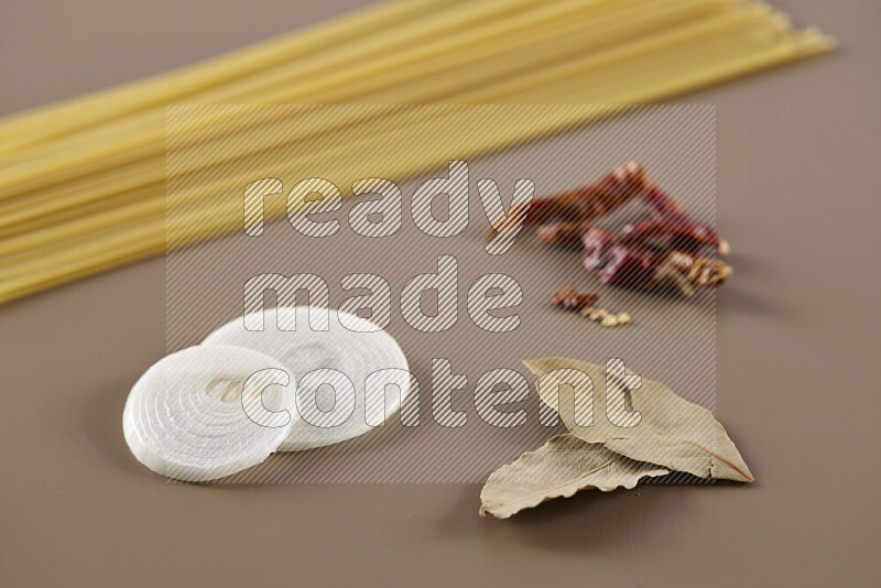 Raw pasta with different ingredients such as cherry tomatoes, garlic, onions, red chilis, black pepper, white pepper, bay laurel leaves, rosemary and cardamom on beige background