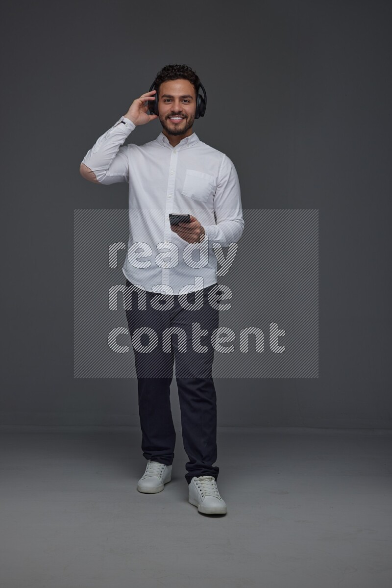 A man wearing smart casual and using his phone and headphone eye level on a gray background