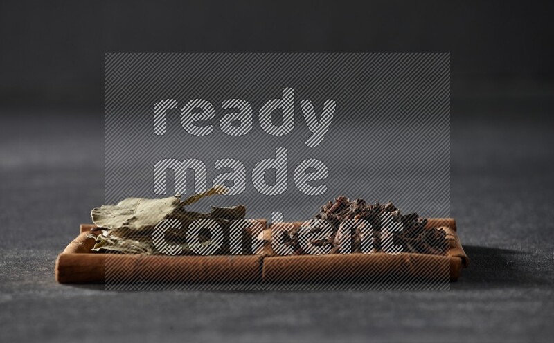 مربعان من أعواد القرفة ممتلئان بالقرنفل وأوراق الغار علي خلفية سوداء