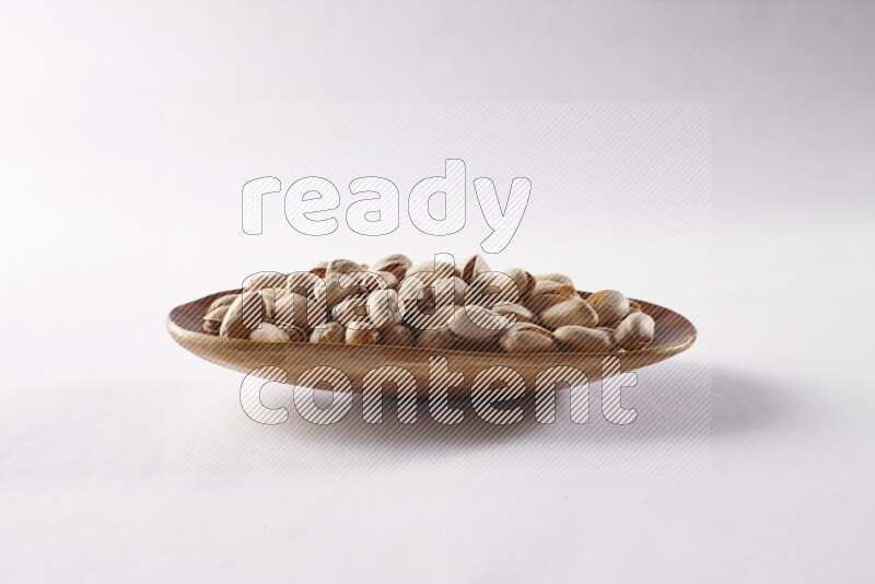 Pistachios in a wooden plate on white background