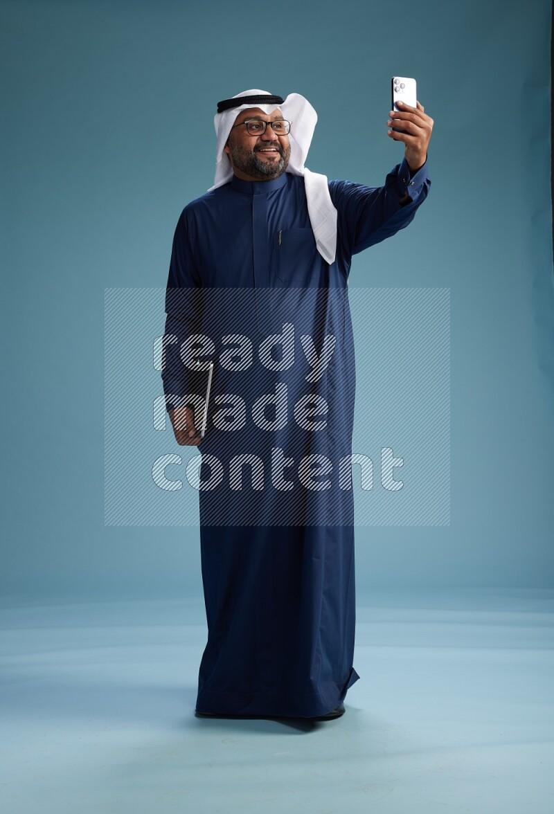 Saudi Man with shimag Standing taking selfie on blue background