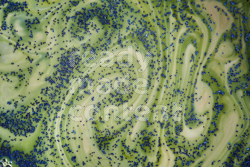 A close-up of sparkling blue glitter scattered on swirling blue and green background
