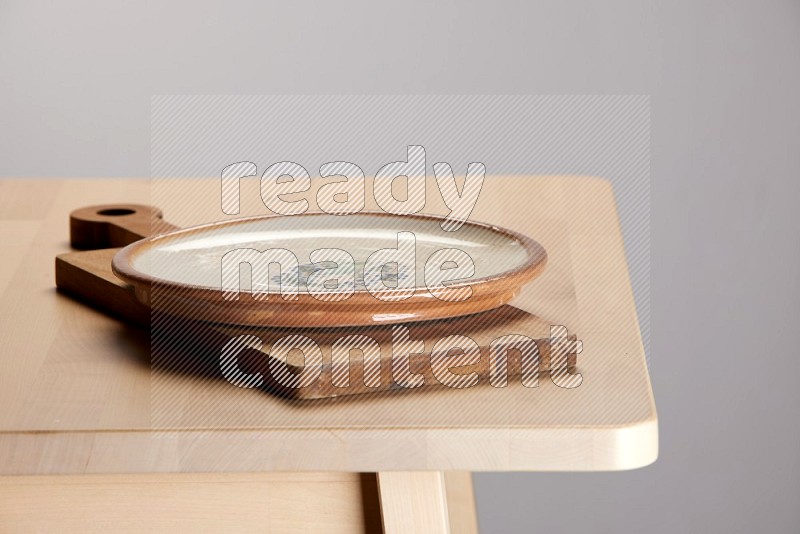 multi-colored pottery Plate placed on a  wooden rectangular cutting board on the edge of wooden table