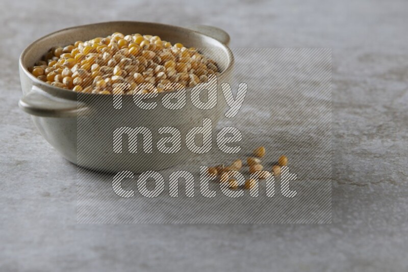corn kernel in a off-white handheld ceramic bowl on a grey textured countertop