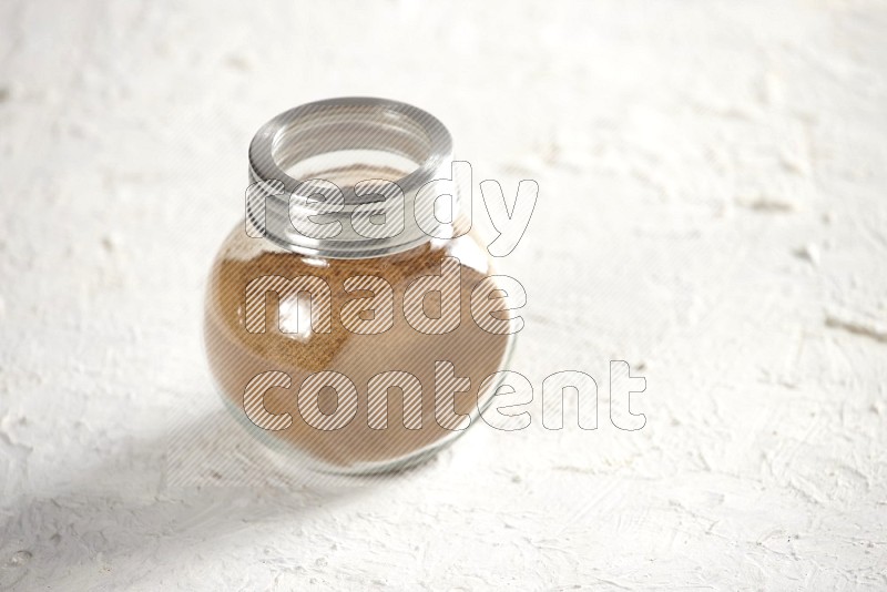 Herbs glass jar full of cinnamon powder on a textured white background