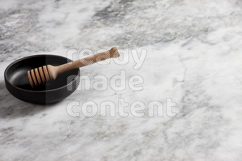 Black Pottery bowl with wooden honey handle in it, on grey marble flooring, 45 degree angle