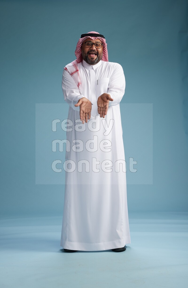 Saudi Man with shimag Standing Interacting with the camera on blue background