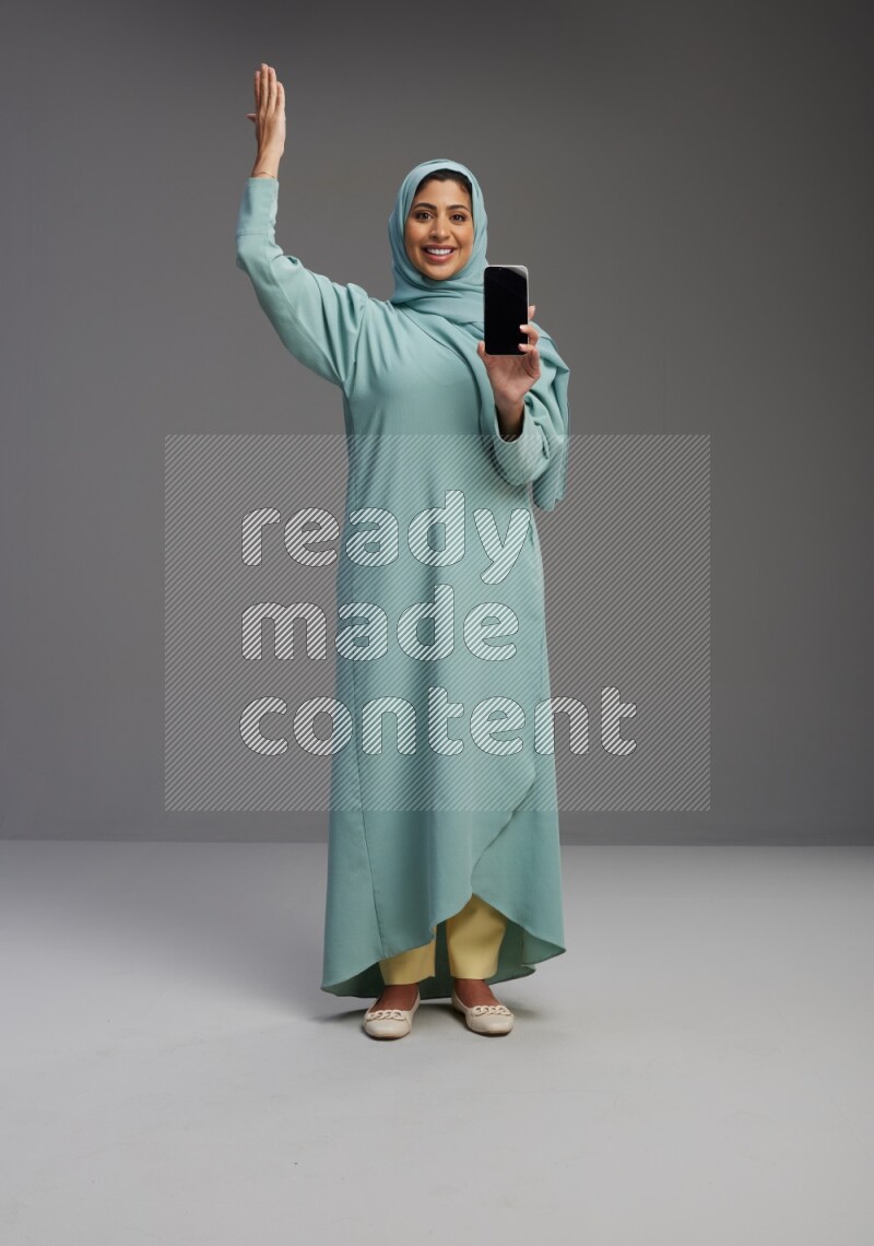 Saudi Woman wearing Abaya standing showing phone to camera on Gray background