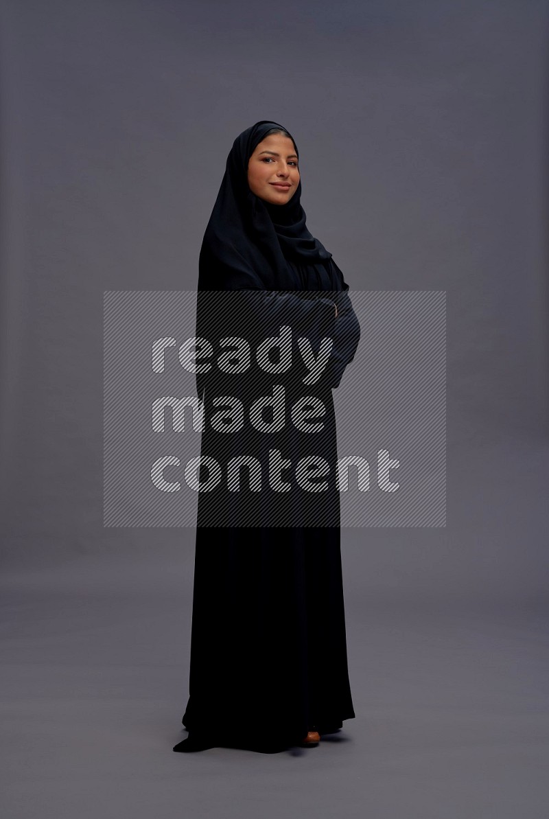 Saudi woman wearing Abaya standing with crossed arms on gray background