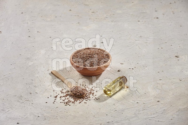 A wooden bowl and spoon full of flax and a bottle of flax oil on a textured white flooring in different angles