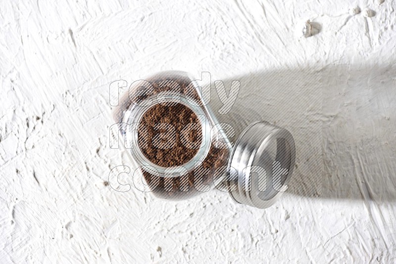 A glass spice jar full of cloves powder on textured white flooring