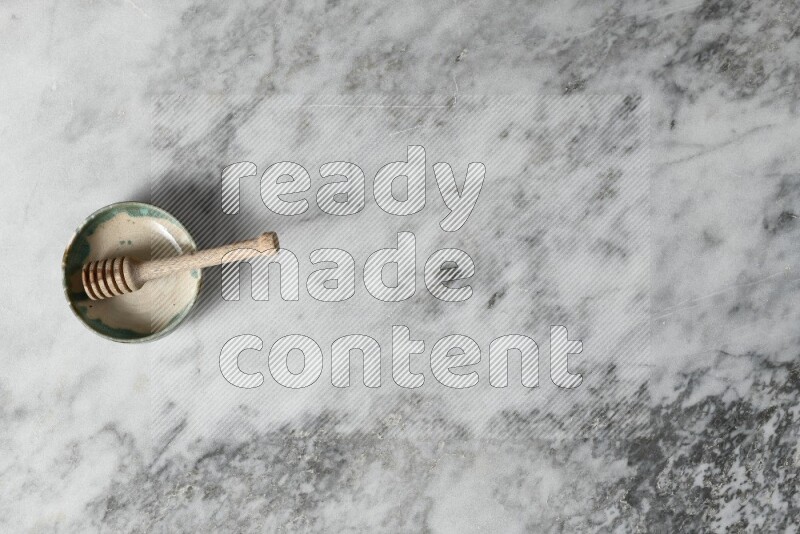 Multicolored pottery bowl with wooden honey dipper in it on grey marble background