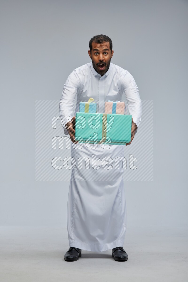 Saudi man Wearing thob standing holding gift box on Gray background