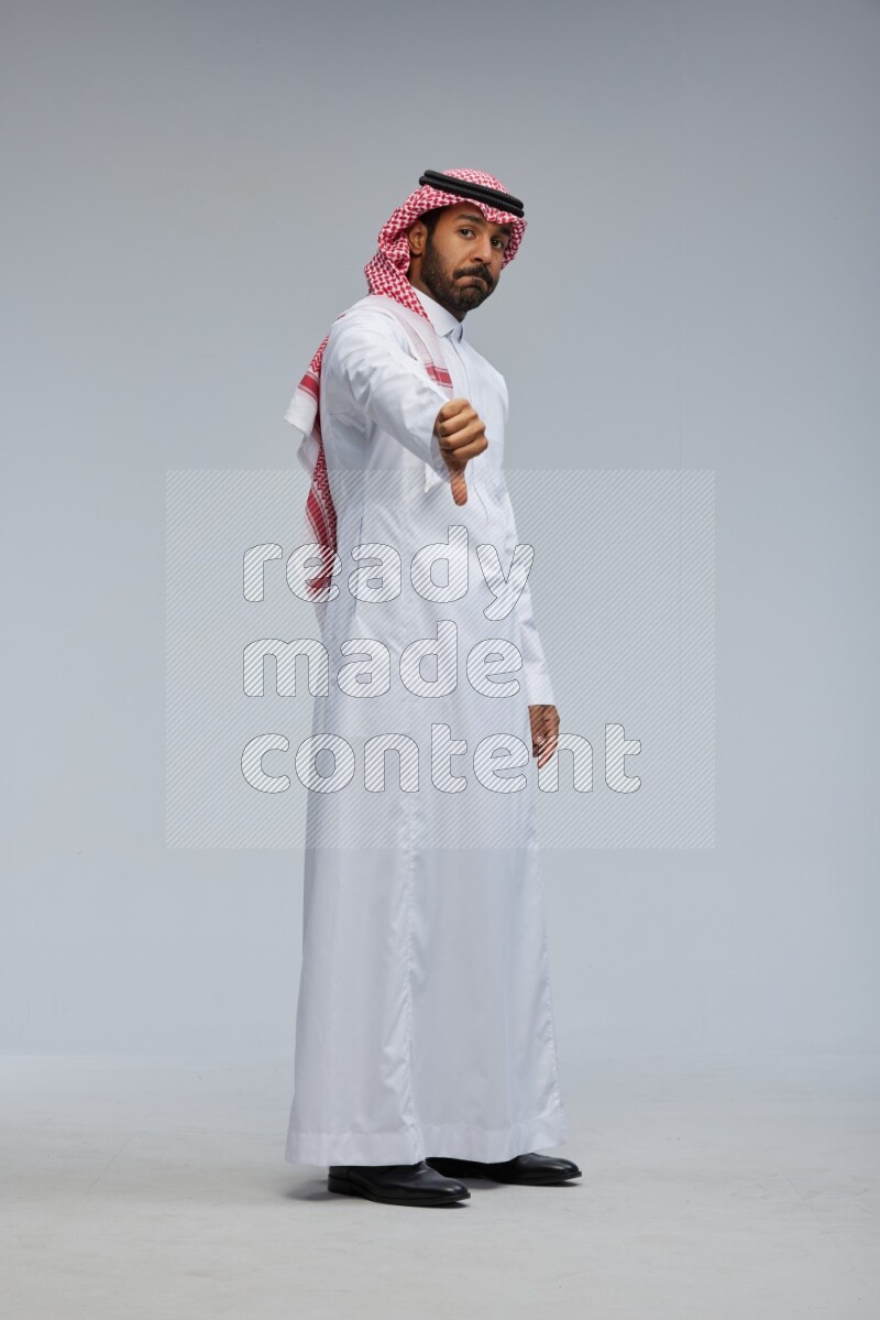 Saudi man Wearing Thob and shomag standing interacting with the camera on Gray background