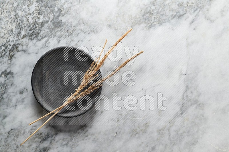 Wheat stalks on Black Pottery Plate on grey marble flooring, Top view