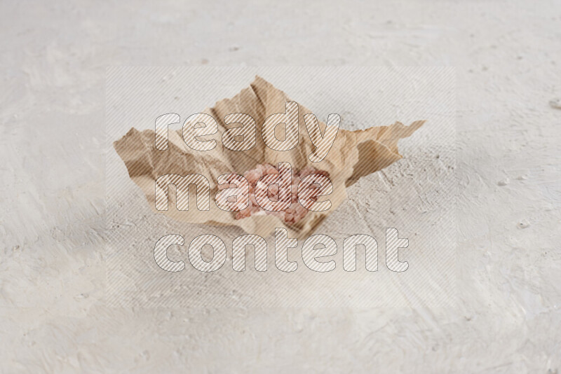 A crumpled piece of paper full of pink himalayan salt on white background