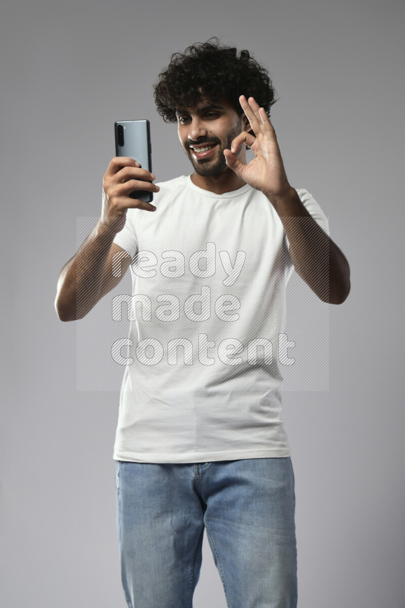 A man wearing casual standing and shooting with his phone on white background