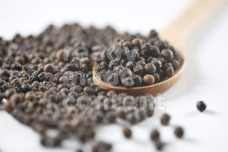 Black pepper beads with wooden spoon on white background