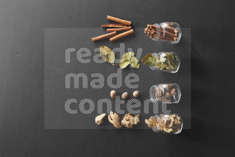 أوراق الغار وزنجبيل مجفف وقرفة وجوزة الطيب في أوعية زجاجية علي خلفية سوداء