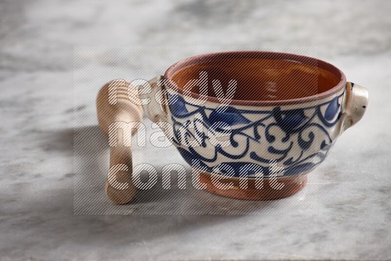 Decorative pottery pot with wooden honey dipper on the side on grey marble background
