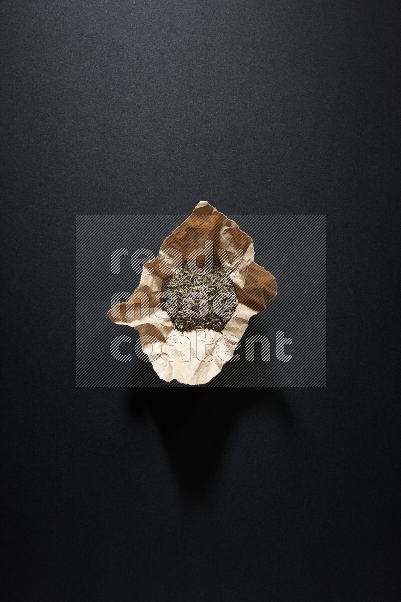 Cumin seeds in a crumpled piece of paper on black flooring