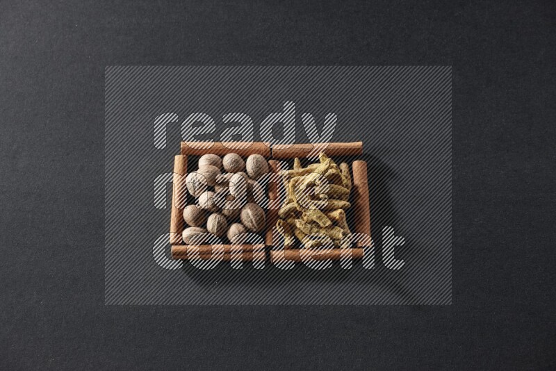 مربعان من أعواد القرفة ممتلئان بجوزة الطيب وأصابع الكركم علي خلفية سوداء