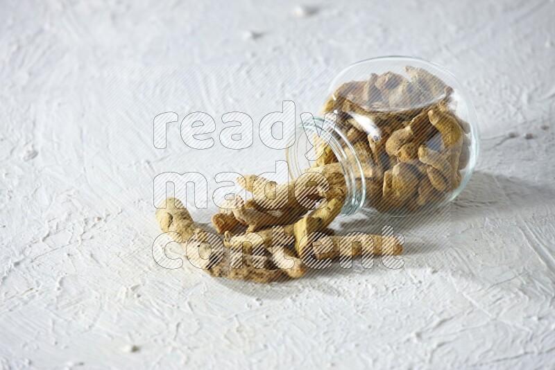 A flipped glass spice jar full of dried turmeric fingers and fell out it on textured white flooring
