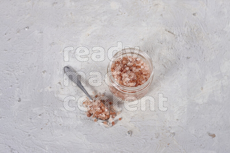 A glass jar full of coarse himalayan salt crystals on white background