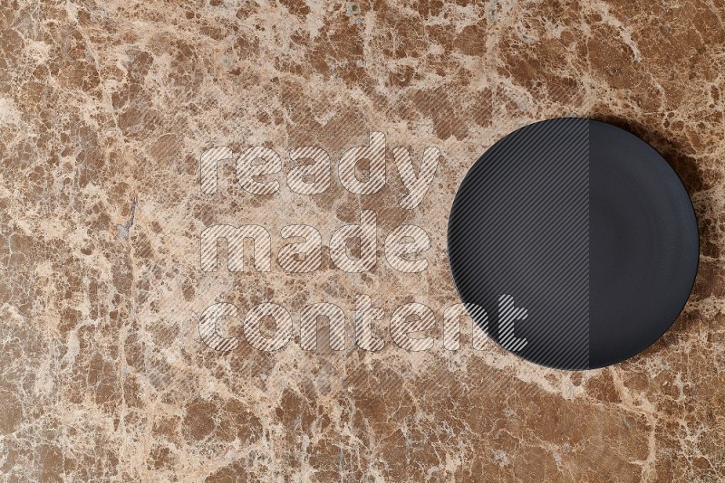 Top View Shot Of A Black Ceramic Circular Plate On beige Marble Flooring