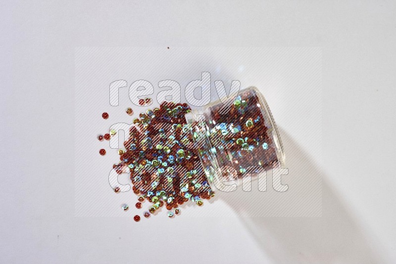 A glass jar full of colored sequins on grey background