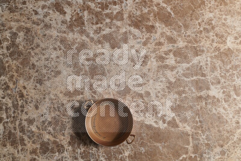 A small copper pan on beige marble background